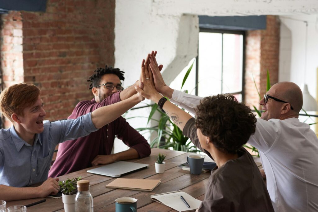 Diverse group of professionals giving a high-five in an office setting, symbolizing teamwork and success.